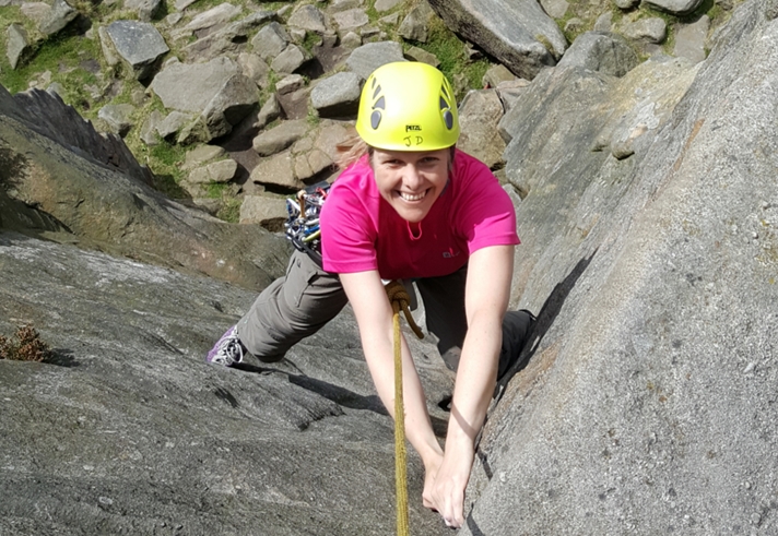 A woman climbing a rock face with a big smile on her face.