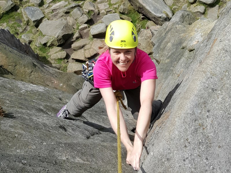 A woman climbing a rock face with a big smile on her face.
