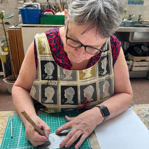 A person working on a piece of artwork on a cutting mat, in a studio.