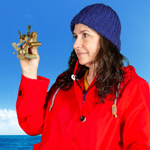 A person, wearing a red raincoat and a blue woolly, holds a small brass sextant.  