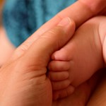 An adult's hand cradling a baby's foot.