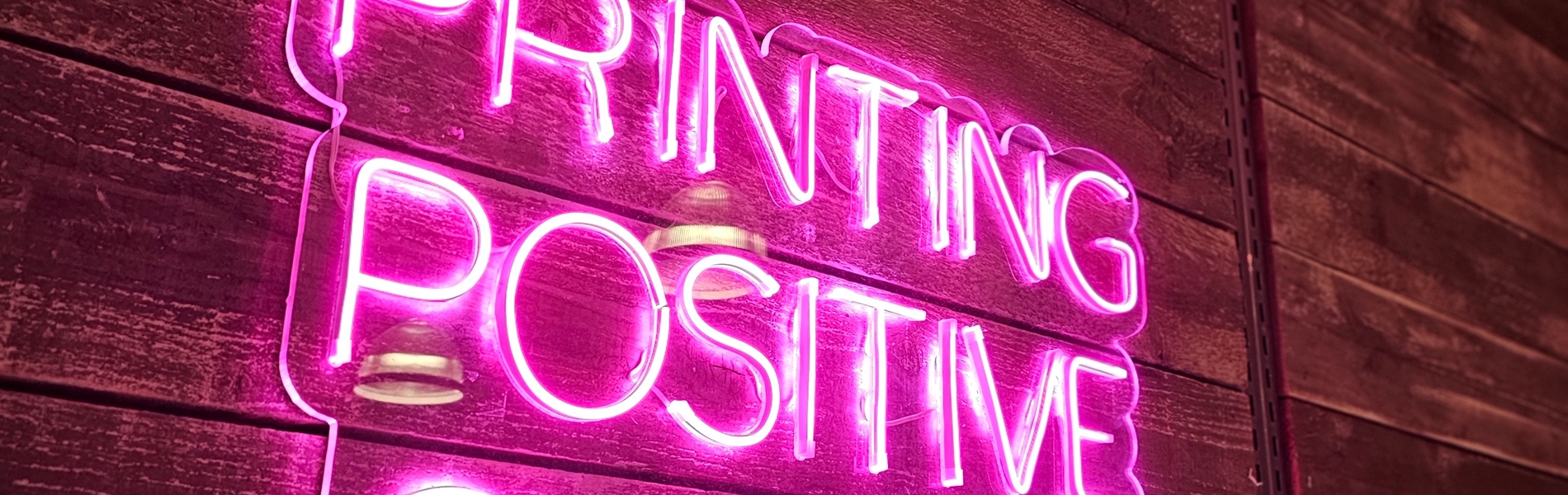 A pink neon sign that reads 'Printing Positive Change'.