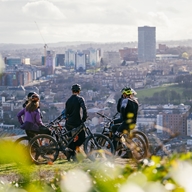 Five people on mountain bikes rest for a moment at the top of Parkwood in Sheffield. In the background you can see the city centre.