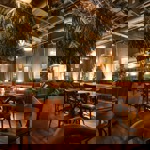 A warmly lit restaurant interior with wooden floors, wooden tables and chairs, large potted plants, and soft ambient lighting, creating a cosy, natural atmosphere.