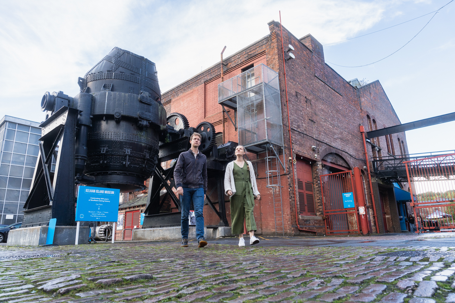 A couple walking in front of the bessemer converter at kelham island museum 