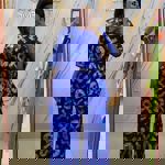 A person wearing a vibrant blue two-piece outfit featuring a loose-fitting top and wide-leg trousers with bold white tie-dye patterns. The outfit is styled in a modern Afrocentric design and displayed in a boutique setting with a marble-effect wall and gold accents in the background.