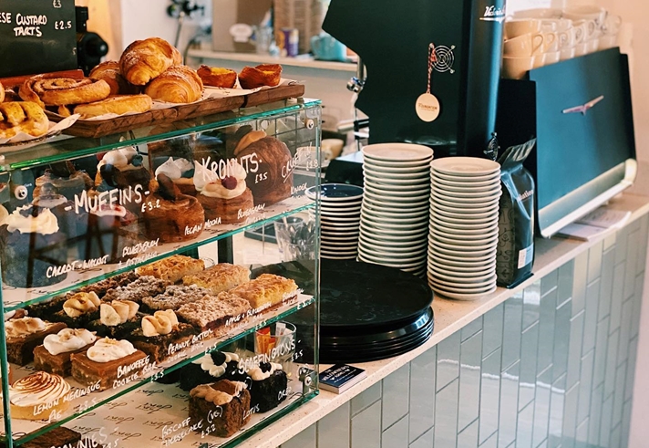 A counter with a coffee machine and a glass case full of pastries.