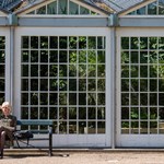 A person sat on a bench outside the Glass House at Sheffield Botanical Gardens.