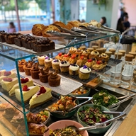 A glass display case on a counter filled with cakes, pastries and salads at Kollective Café.