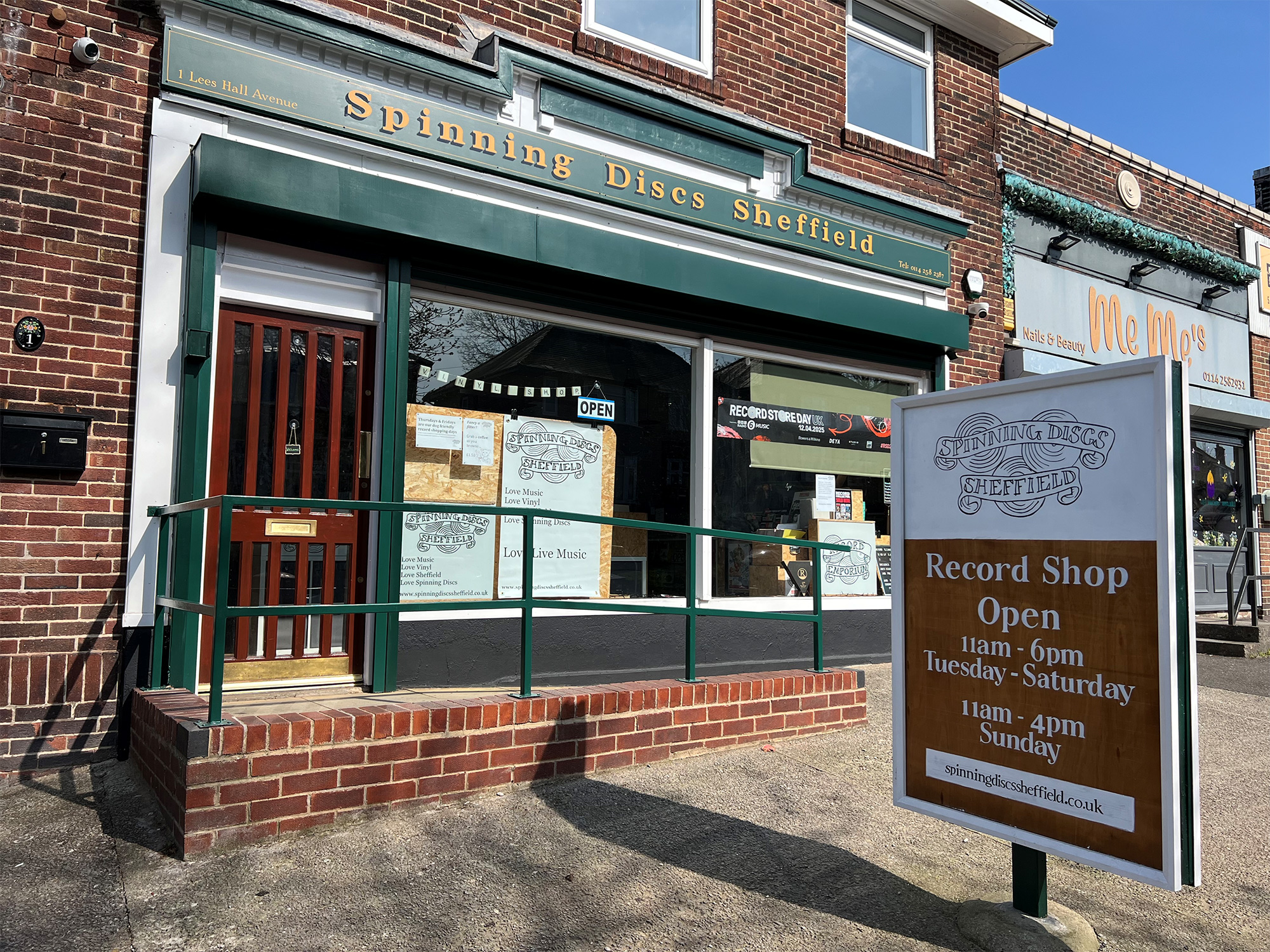 Exterior view of a brick-fronted record shop named “Spinning Discs Sheffield.” The shop has a green awning and large windows with posters and signs. 
