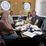 A group of people sat round a large table, writing letters.