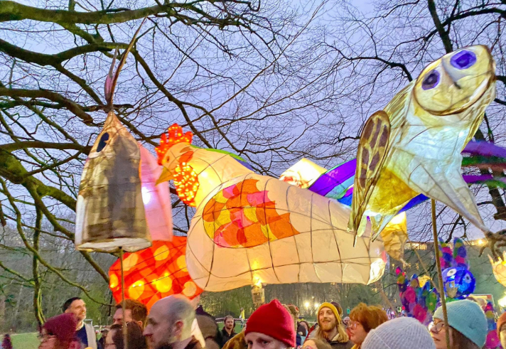 Crowds of people, holding hand-made lanterns aloft, walking in a parade. 
