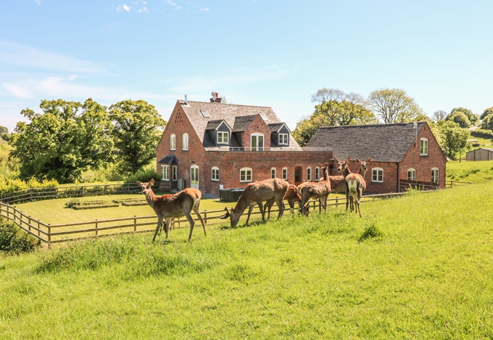 Exterior view of a Sykes Holiday Cottage with front garden and countryside surroundings.
