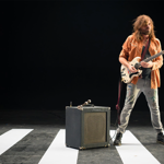 Evan Dando, of The Lemonheads, stood next to an amp, playing a white guitar.