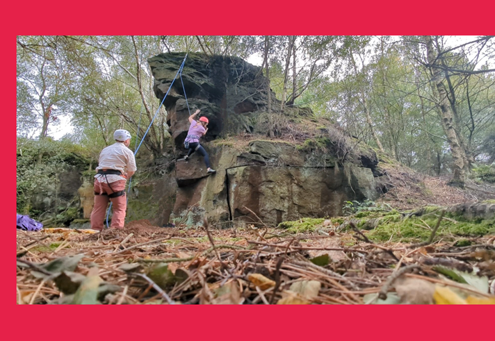 Two people bouldering at a rocky outcrop in the woods.