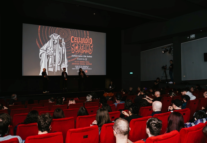Cinema seen from the back with rows of audience sat in front of a screen with Celluloid Screams branding on it