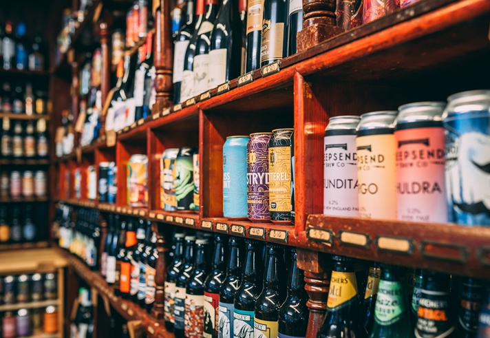A store shelf filled with a wide variety of alcoholic beverages, including colorful cans and neatly arranged bottles of beer. Additional shelves in the background display more drink options, suggesting a large selection.