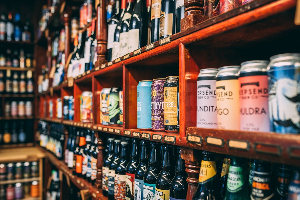 A store shelf filled with a wide variety of beers, including colorful cans and neatly arranged bottles. Additional shelves in the background display more  options, suggesting a large selection.