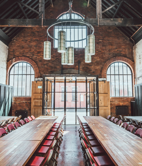 Rustic-style meeting room with exposed brick walls, wooden beams, and a long rectangular wooden table surrounded by chairs. 