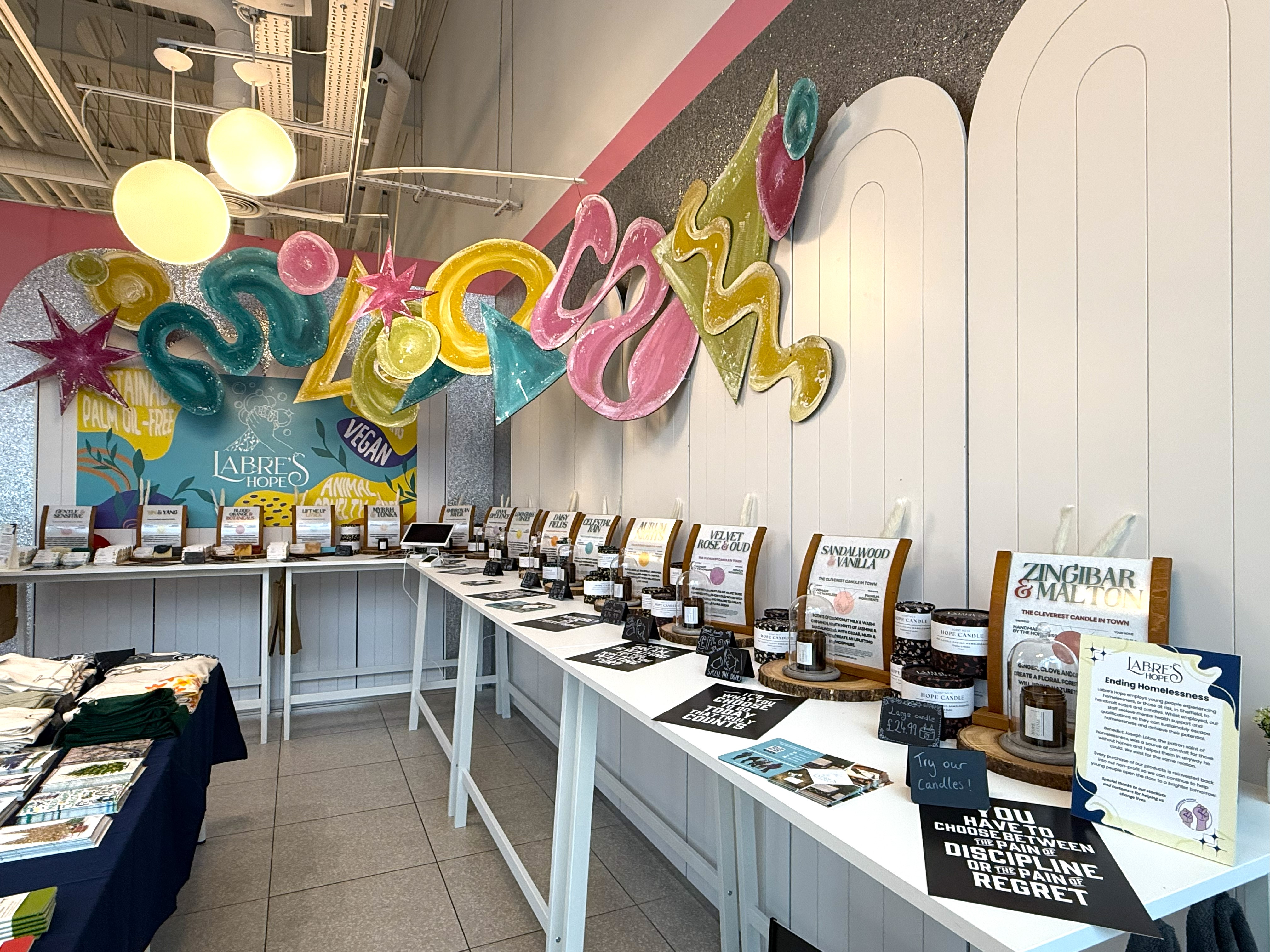 Display table inside the pop-up market showcasing rows of jars and informational cards about products, with colorful signage and decorative wall art in the background