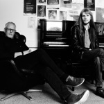 A black and white image of two people sat next to a piano.
