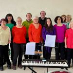 The members of Nether Edge Voices standing around a keyboard on a stand.