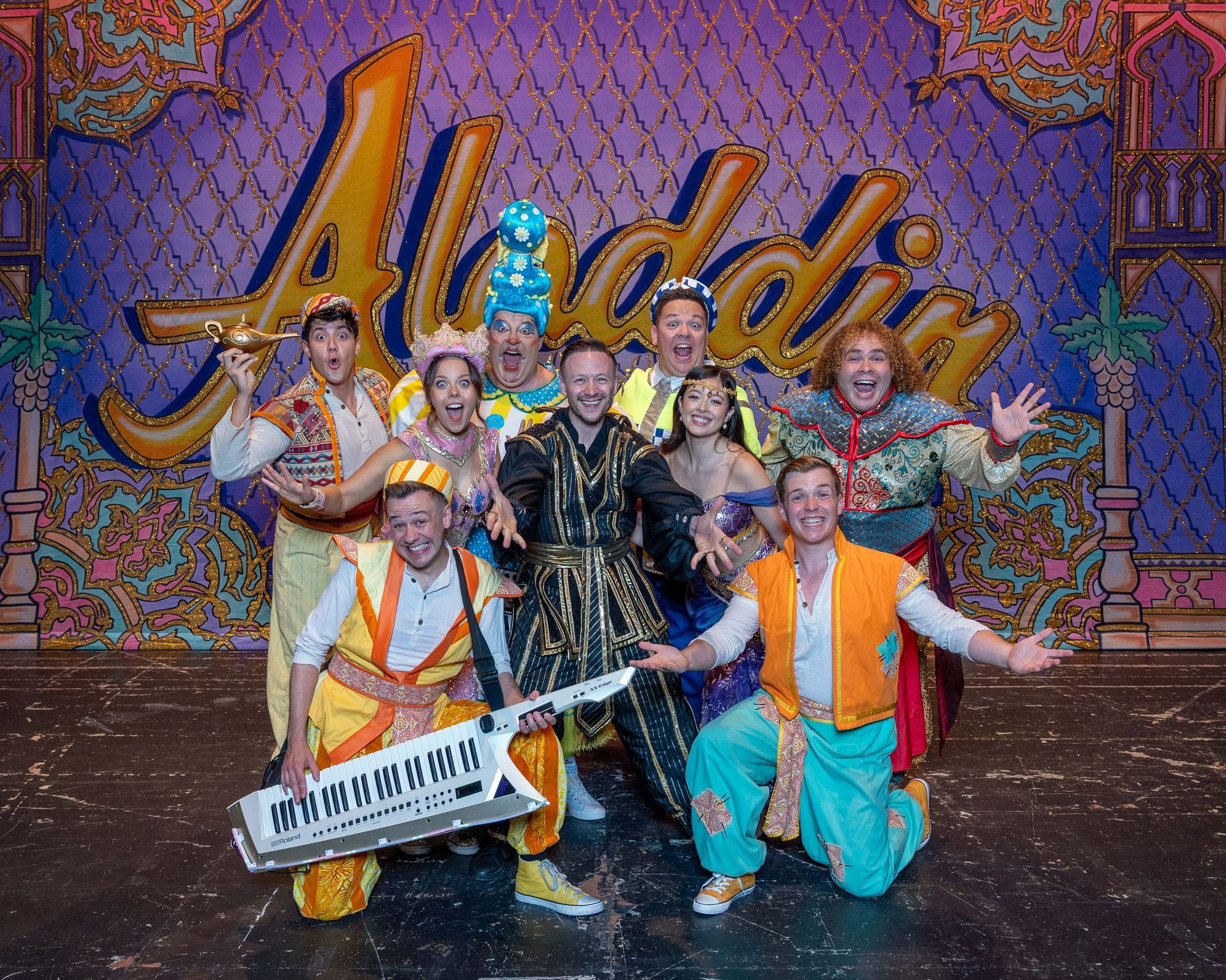 The cast of the Lyceum Panto Aladdin pose in a group shot with arms wide and joyful expressions