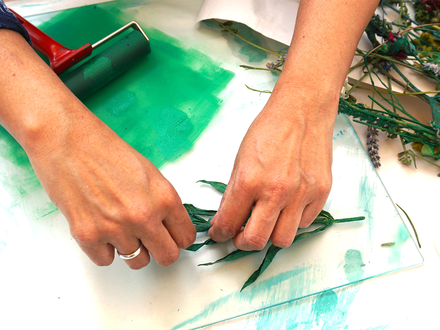 A close-up of someone's hands who is creating a print using inks and plant leaves.
