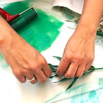 A close-up of someone's hands who is creating a print using inks and plant leaves.