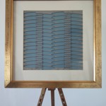 Framed artwork with a gold frame showcasing a blue background and metallic cut-out shapes arranged in vertical rows, displayed on a wooden easel.