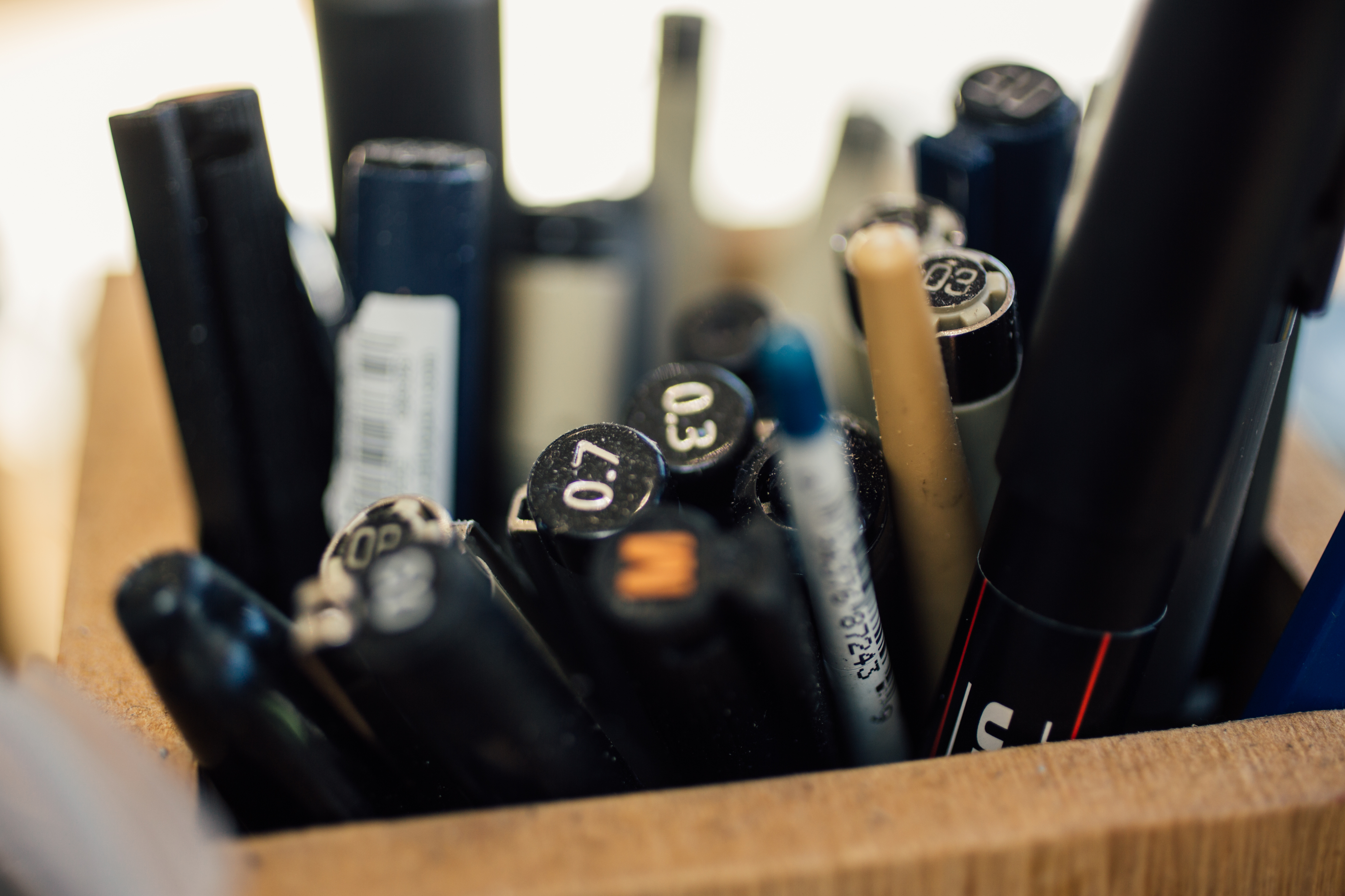 A close up of a wooden pot full of pens and pencils.