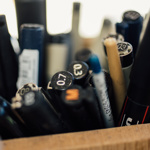 A close up of a wooden pot full of pens and pencils.