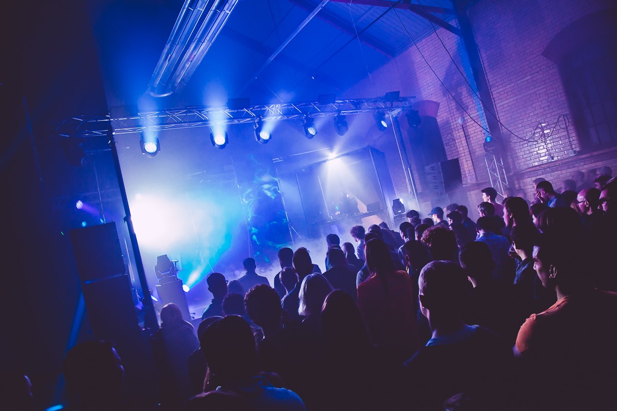 A crowd of people listening to music and dancing in a dark nightclub.