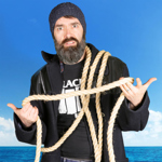 A person in a donkey jacket, with a large beard, holds a length of rope whilst looking bemused.