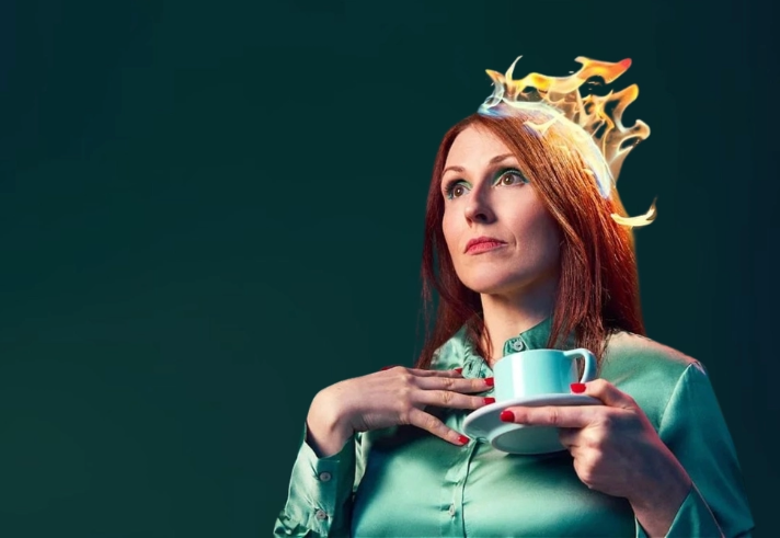 A woman, looking distracted, in a green dress holding a cup of tea. There are flames on her hair.