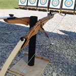 Two bows on a stand, in the distance is a row of archery targets.