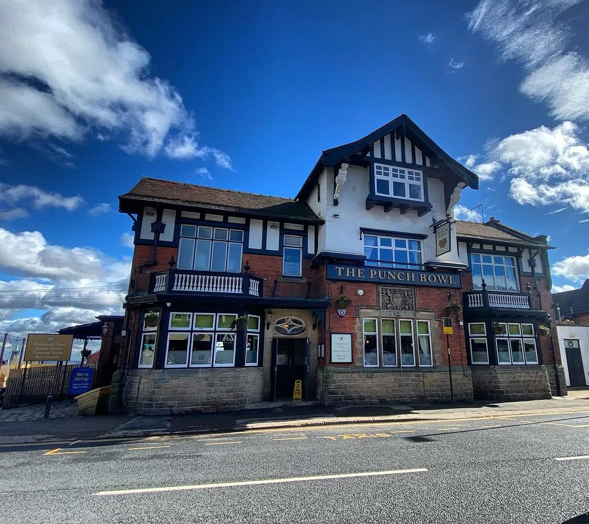 The exterior of The Punch Bowl pub in Crookes, a large traditional brick building with white and black timber detailing, set against a bright blue sky.