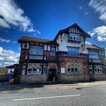 The exterior of The Punch Bowl pub in Crookes, a large traditional brick building with white and black timber detailing, set against a bright blue sky.