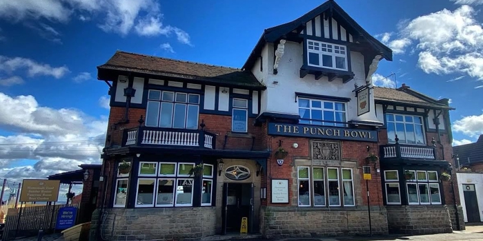 The exterior of The Punch Bowl pub in Crookes, a large traditional brick building with white and black timber detailing, set against a bright blue sky.