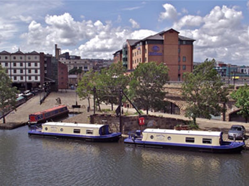 A view of Victoria Quays and the canal basin in the centre of Sheffield on a sunny day. There are several narrow boats moored up.