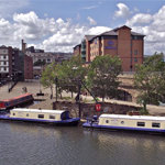A view of Victoria Quays and the canal basin in the centre of Sheffield on a sunny day. There are several narrow boats moored up.