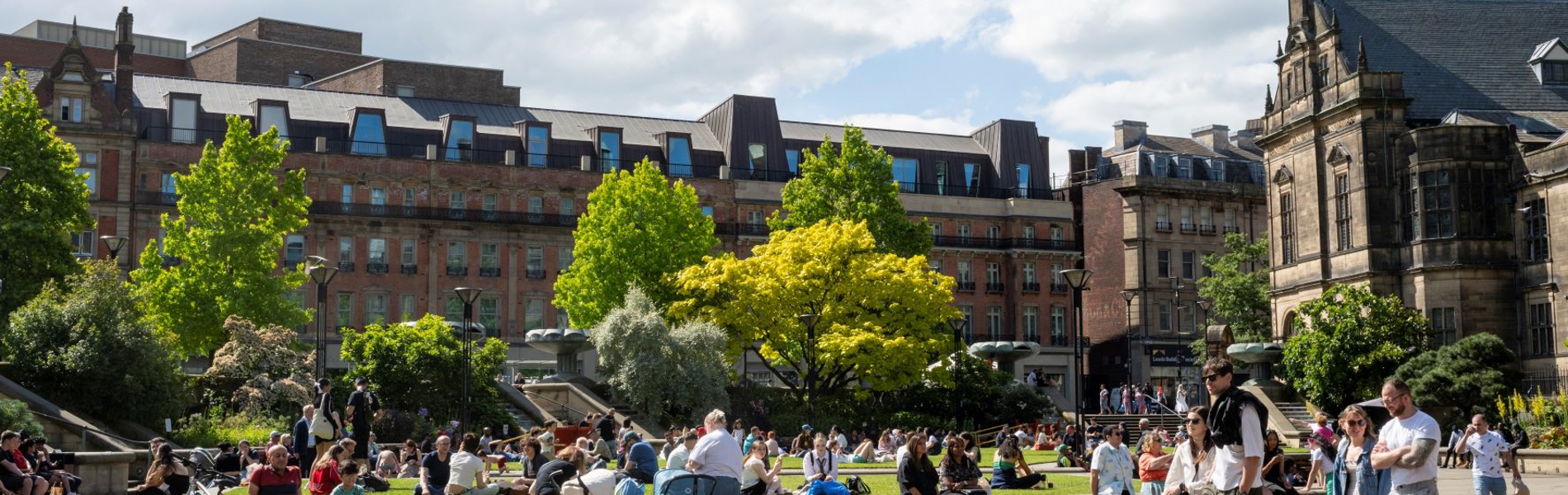 Lots of people enjoying a warm sunny day in The Peace Gardens. In the background is The Radison Blu Hotel.