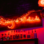 Red neon sign, above a bar, that reads 'Sidney & Matilda'.