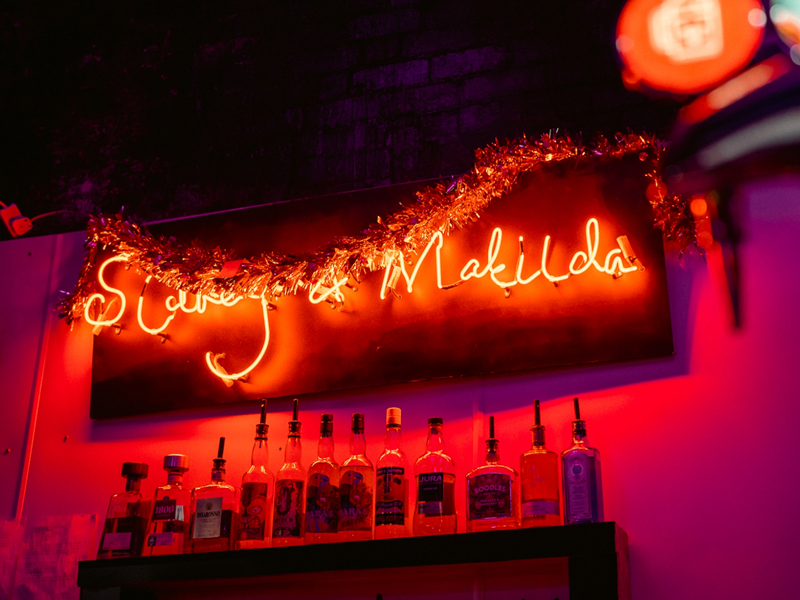 Red neon sign, above a bar, that reads 'Sidney & Matilda'.