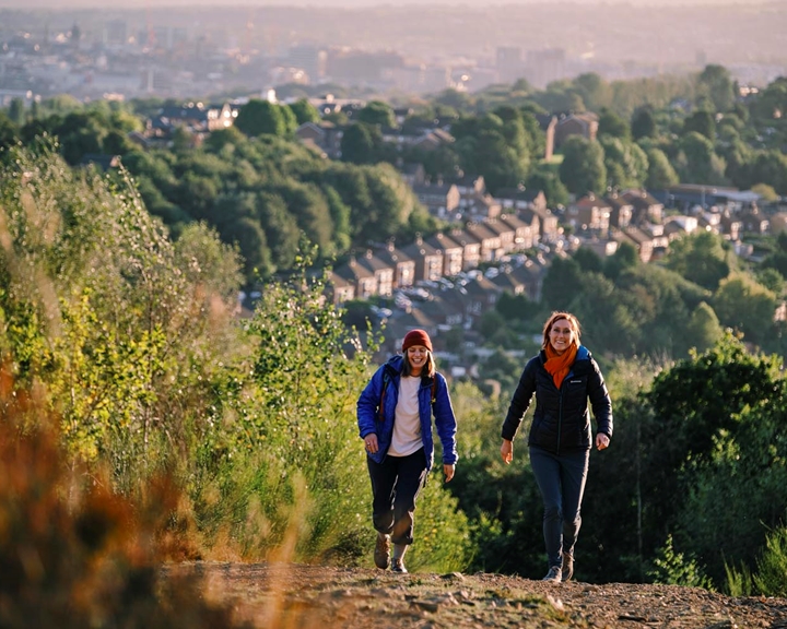 Two people walking in the hills above Sheffield. In the distance you can see rows of houses and the city skyline.