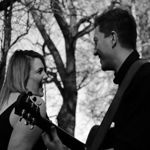 A black and white picture of two people performing; one singing and the other playing a classical guitar.