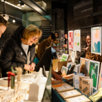 A split image; one side shows people browsing a stall, the other side shows a stall selling prints and cards.