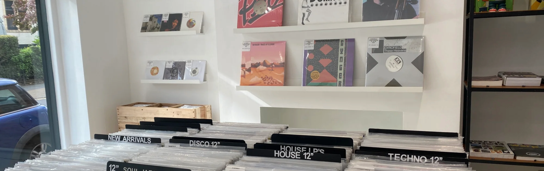 Inside a small record shop you can see racks of vinyl and records displayed on the wall. The shop decor is white and minimalist.