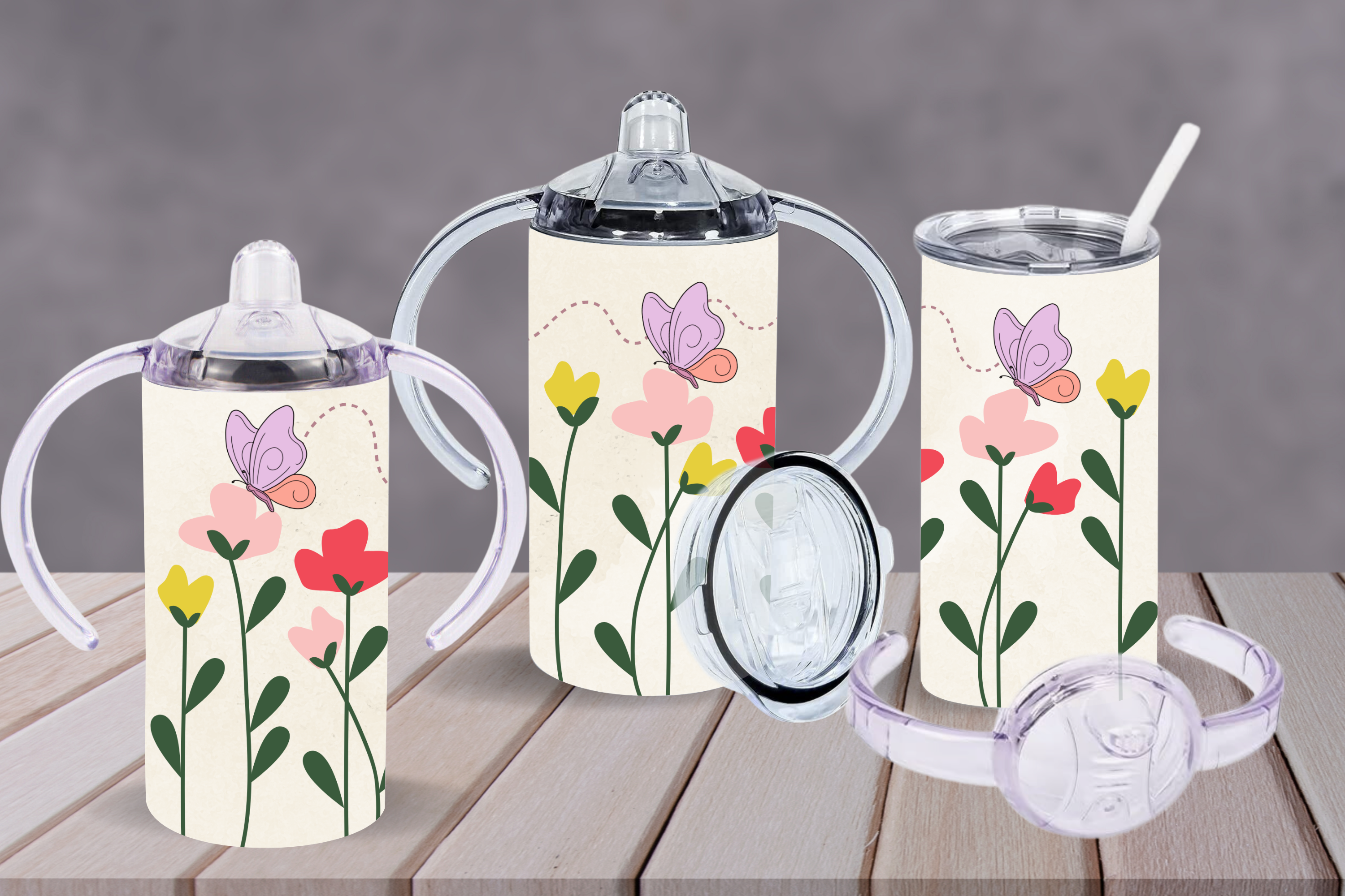 Three drinkware items with interchangeable lids and handles, decorated with a minimalist floral design of pink, yellow, and red flowers with green stems, and purple butterflies on a cream background. The set includes a sippy cup, a tumbler with a straw, and a cup with handles.