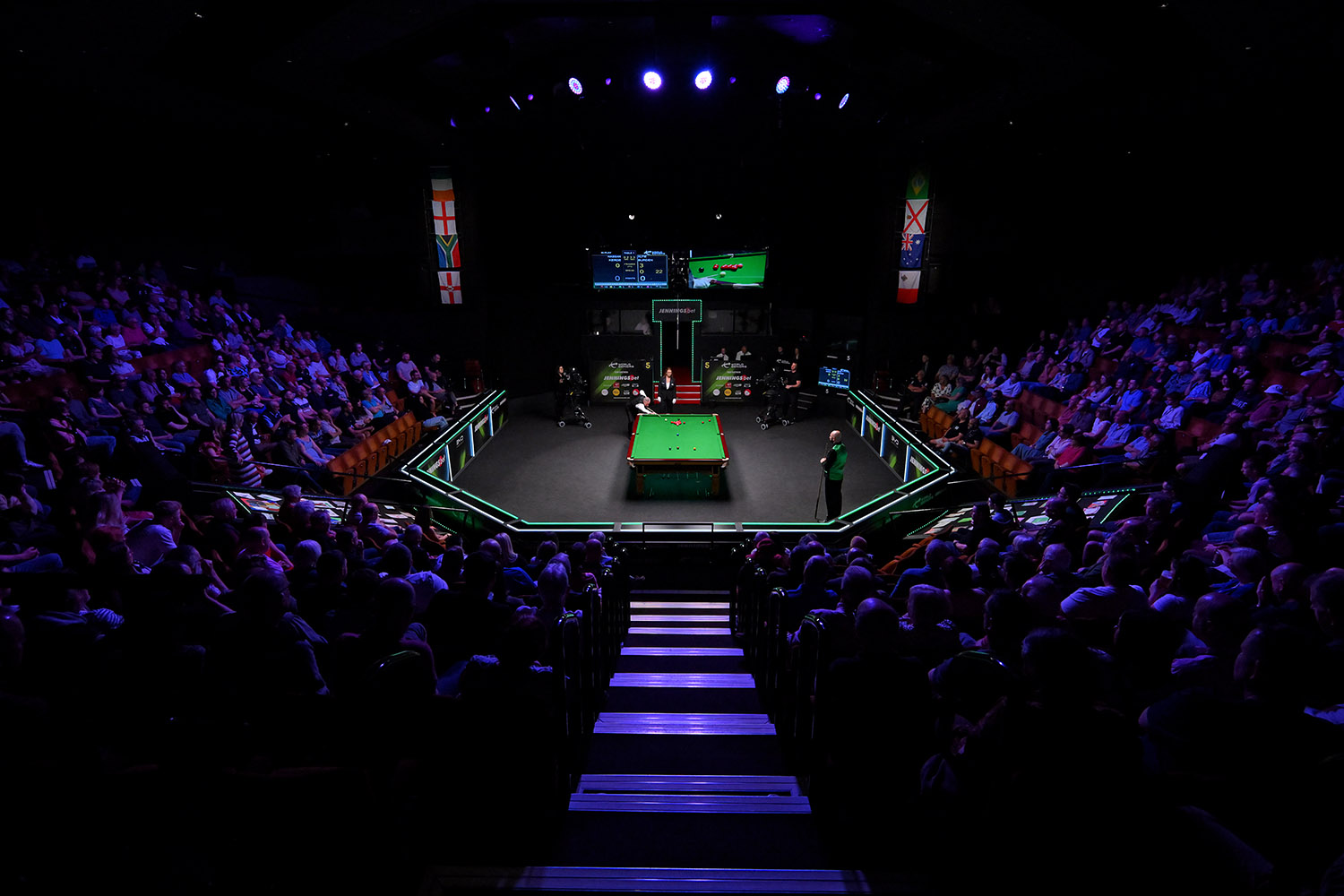 a spotlight shines on a snooker table in the middle of a darkened auditorium as two snooker players get ready for a match